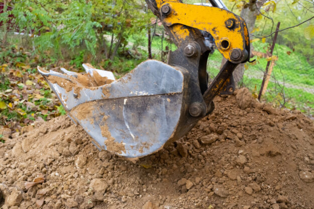 The excavator shovels earth with clay from the pit with a bucket for the construction of a septic tank. Ground work of the machine HYDRAULIC SYSTEM CONTAMINATES & FAILURE TYPES